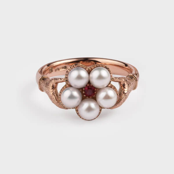 A bespoke ring in rose gold, showing two metal hands holding a flower made of pearls and a ruby in the centre.